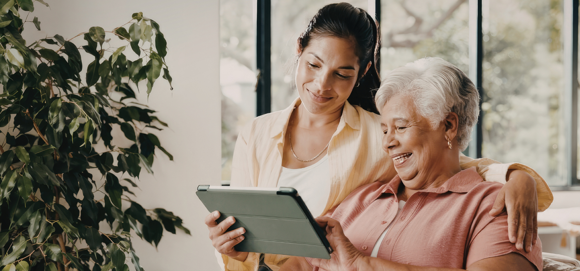 A caregiver and senior woman smiling at a tablet together
